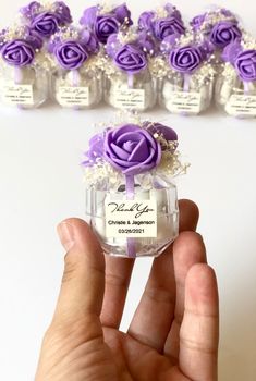 a hand holding a small glass bottle with purple roses in it