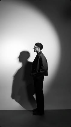 a man standing in front of a white wall with a shadow on the wall behind him