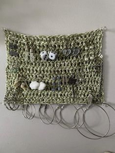 a crocheted wall hanging with lots of rings attached to it and some earrings