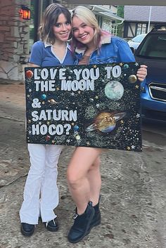 two women holding up a sign that says love you to the moon and saturn hoco