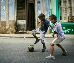 two young boys playing with a soccer ball on the street in front of an old building