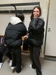 two women standing in front of a mirror talking to each other while one woman covers her mouth