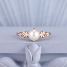 a white pearl and diamond ring sitting on top of a box