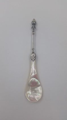 a silver spoon with a pearl in it on a white surface, the spoon is shaped like a tear