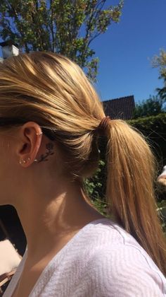 a woman with her hair in a ponytail has tattoos on her left side of her ear