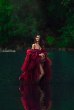 a woman in a red dress is standing in the water with her arms around her body