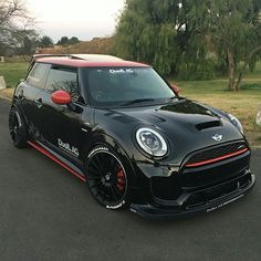 a small black car parked on the side of a road next to some grass and trees