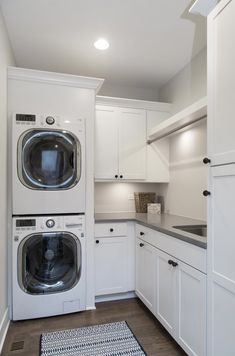 a washer and dryer in a white laundry room with cabinets on either side