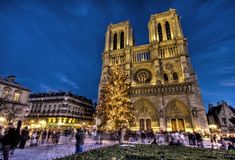 a large cathedral with a lit christmas tree in front of it at night and people walking around