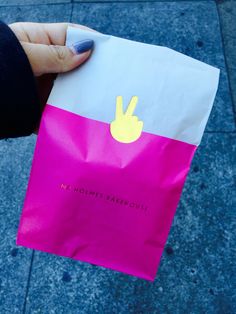 a hand holding a pink and white bag with a yellow peace sign on it's side