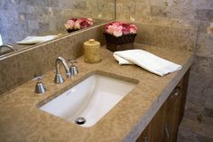 a bathroom sink sitting under a mirror next to a counter top with flowers on it