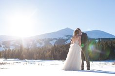 a bride and groom standing in the snow with mountains in the background at their wedding