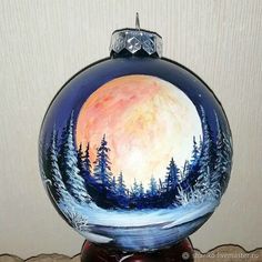 a painted glass ball ornament with trees and the moon on it's side