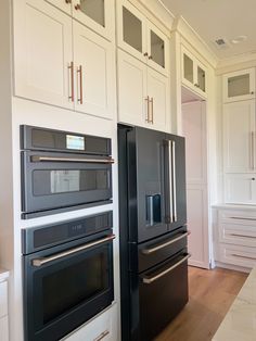 a kitchen with white cabinets and black ovens in the center, along with wooden flooring