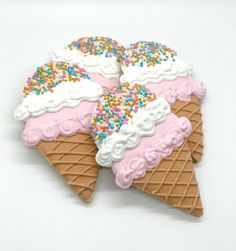 three ice cream cones decorated with sprinkles and frosting on white background