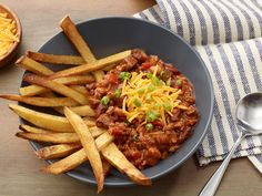 a bowl filled with chili and french fries on top of a table next to a spoon