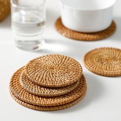 four wicker coasters on a white surface with water in the glass behind them