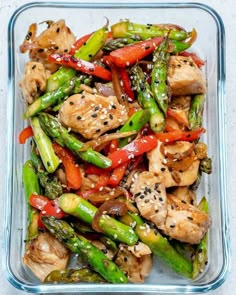 chicken and asparagus stir fry in a glass dish with sesame seeds on top