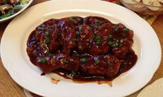 a white plate topped with meat covered in sauce and garnished with green onions