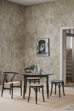 a dining room table and chairs in front of a wall with a painting on it