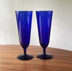 two blue glass vases sitting on top of a wooden table next to each other