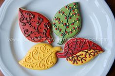 four decorated leaf cookies on a white plate