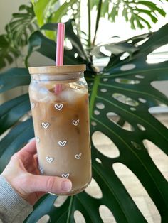 a person holding up a drink in front of a plant with hearts drawn on it