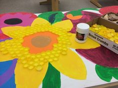 the table is covered with yellow and pink flowers on it, next to a box of paint