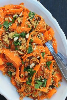 a white plate topped with carrots and nuts next to a silver fork on top of a wooden table