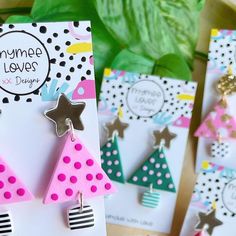 three pairs of earrings are on display in front of some green leaves and pink polka dot cards