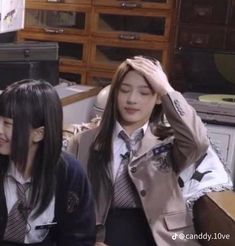 two young women sitting next to each other in front of a computer desk, one holding her head