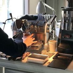 a person is making something in a coffee machine at a counter top with other items on it