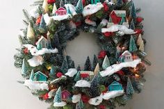 a christmas wreath is hanging on the wall with small trees and houses in front of it