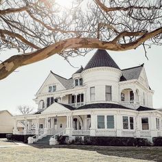 a large white house sitting on top of a lush green field next to a tree