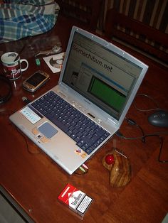 an open laptop computer sitting on top of a wooden desk next to a mouse and cell phone