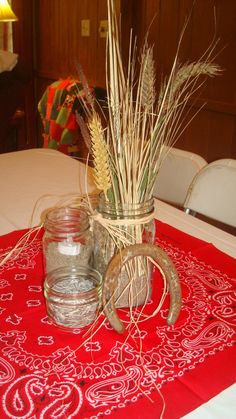 a table topped with two mason jars filled with water and wheat stalks on top of a red table cloth