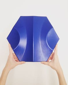 two hands holding up a blue object in the shape of a hexagonal structure