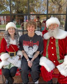 three people dressed as santa claus sitting on a bench in front of a store window