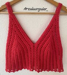 a red crocheted top hanging on a wooden hanger with the word,'art