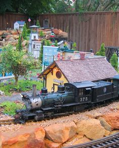 a model train is on the tracks next to a small building and trees in the background