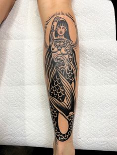 a woman's leg with a black and white tattoo design on it, featuring a mermaid