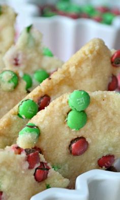 some cookies with green and red candies on them are in a white bowl next to other desserts