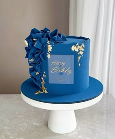 a blue birthday hat with gold flowers on it sitting on a white cake platter