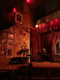 a room with red curtains and pictures on the wall, some chairs and tables in front of them