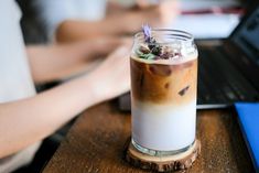 a glass filled with liquid sitting on top of a wooden table next to a laptop