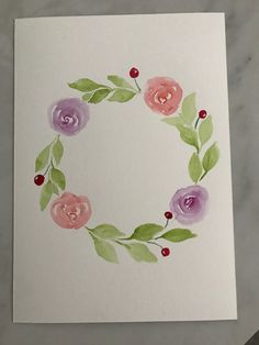 a watercolor painting of flowers and leaves in a circle on a white paper background