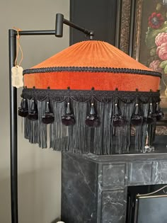 an orange and black lamp with tassels on it next to a fireplace mantel