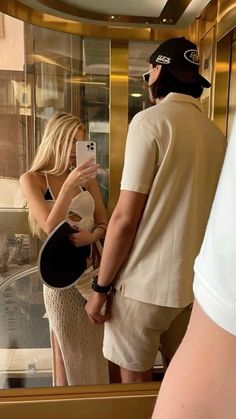 a man and woman standing in front of a window looking at their cell phones together