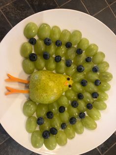 a white plate topped with grapes and a green bird next to a pear on top of it