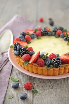 a cake topped with berries and cream on top of a pink plate next to a spoon